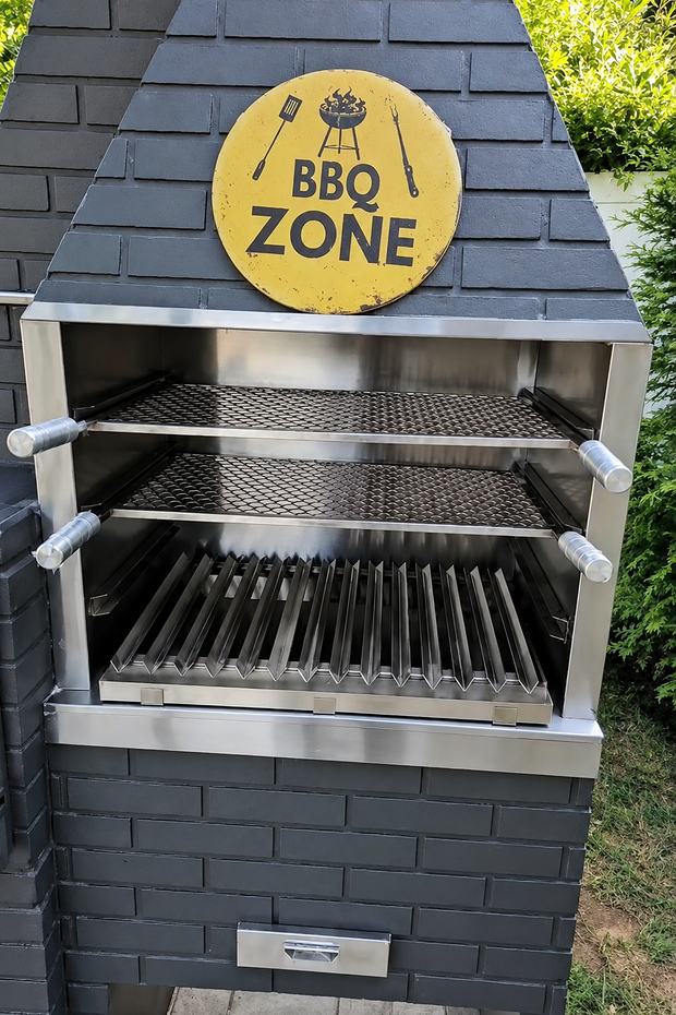 Detalhe da boca da churrasqueira BBQ Zone: moldura em aço inox, duas grelhas superiores reguláveis e grelha inferior com aletas.