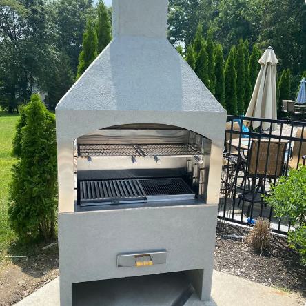 Churrasqueira BBQ Zone com acabamento claro e chaminé, instalada ao lado de uma área de piscina cercada.
